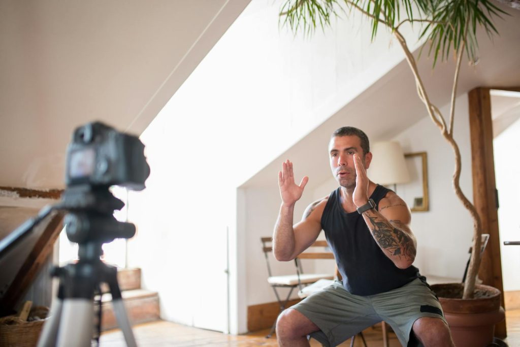 Tattooed man filming a workout video indoors, focusing on exercise technique.